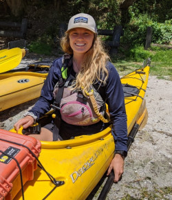 Cady sitting in a yellow kayak on the sandy shore. 